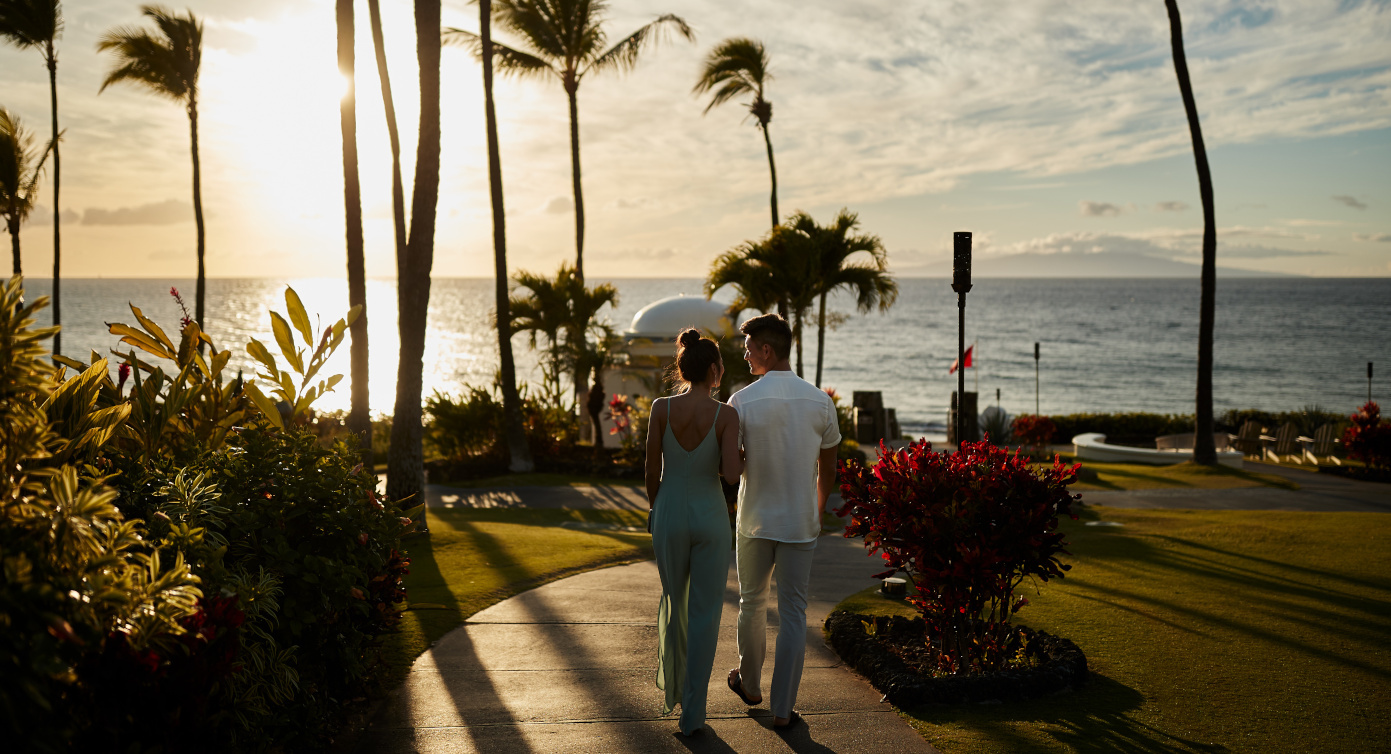 a couple walking towards a beach at sunset