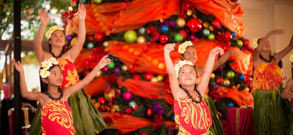 hula dancers dancing in front of a large christmas tree