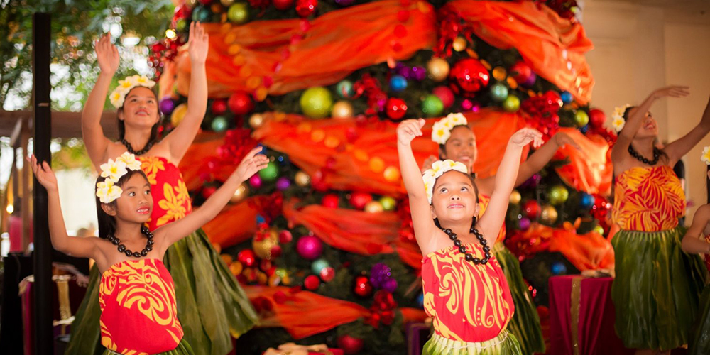 hula dancers dancing in front of a large christmas tree
