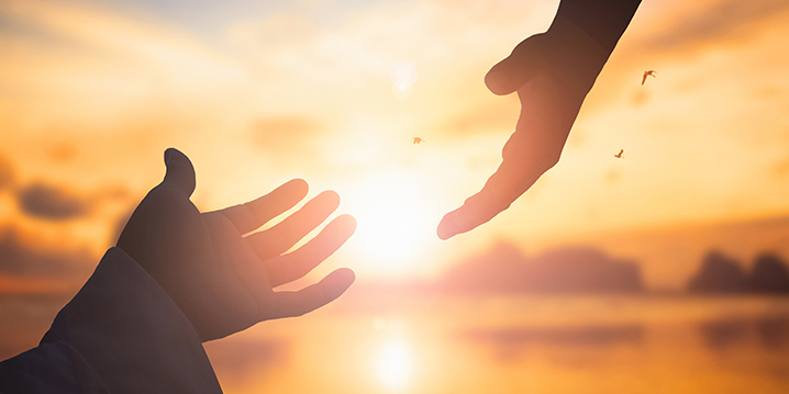 two hands about to touch at sunset